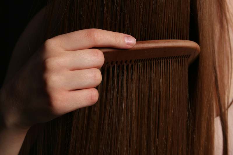 Close-up of hands holding a UV-protective hair oil bottle with sunlit hair in background